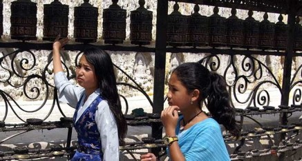 年青的女孩在尼泊爾的斯瓦揚布那斯佛塔轉動祈禱輪。