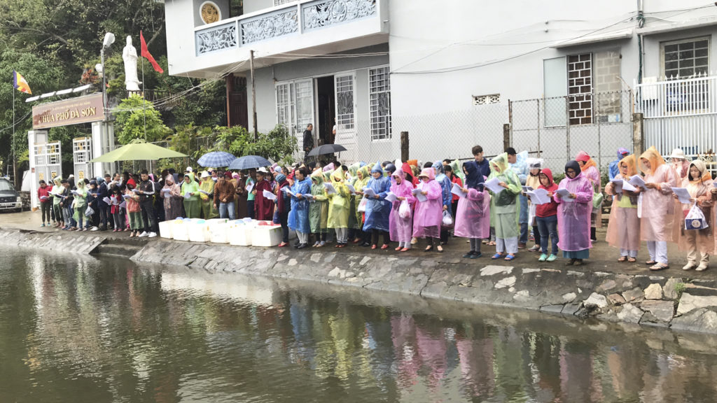Disciples stand in the rain at the CoCo River for ceremony to liberate captive living beings after the Kuan Yin Empowerment in Da Nang, Vietnam.